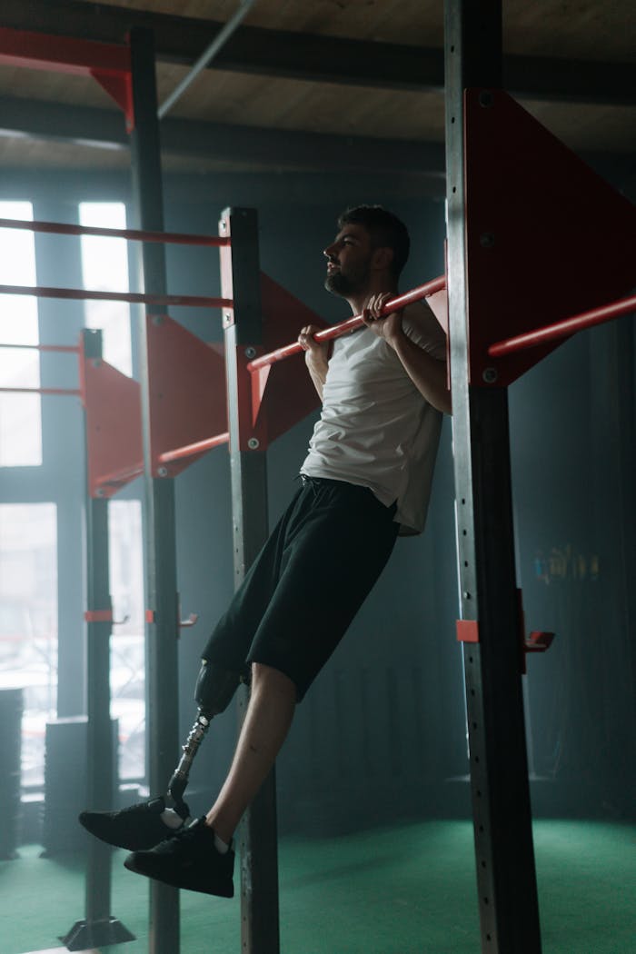 A determined man with prosthetic leg working out on pull-up bars in a gym setting.